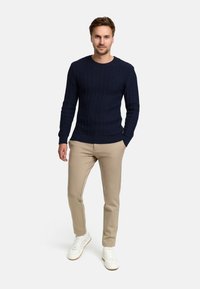 Marineblauwe ribgebreide trui met een ronde hals, gecombineerd met beige slim-fit broeken en witte sneakers. Casual outfit met textielstof.