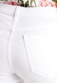 Vaqueros de mezclilla blanca con una textura lisa, que cuentan con dos bolsillos traseros y un diseño ajustado. La costura es sutilmente visible.