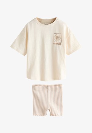 Trumpomis rankovėmis kreminės spalvos marškinėliai su saulės atvaizdu ir užrašu „Le Soleil“, derinami su kreminiais ir smėlio spalvos vertikaliomis dryžuotomis medžiaginėmis šortais.