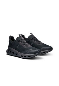 Schwarze Sportschuhe mit Mesh-Obermaterial, strukturiertem Design und dickem, gepolstertem Sohlenprofil, das kreisförmige Aussparungen für Luftzirkulation und Flexibilität aufweist.