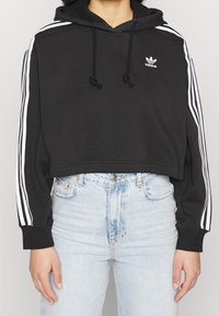 Svart kortärmad hoodie med drarem i huvan, med vita tre-stripes accenter längs ärmarna och en broderad Adidas-logga på bröstet.