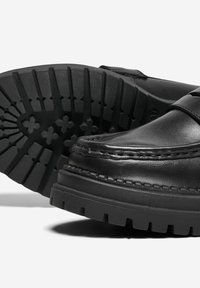 Scarpe in pelle nera con punta tondeggiante, dettaglio di cuciture in rilievo e suola in gomma testurizzata con scanalature profonde per una buona aderenza.