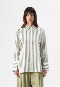 Button-up shirt in cream with black vertical stripes, featuring a collar, long sleeves, and cuffs with striped accents. Smooth texture.