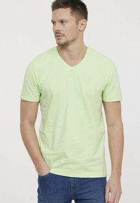 T-shirt en coton vert clair avec des manches courtes et un col en V. Présente un design minimaliste avec un petit logo sur la poitrine.
