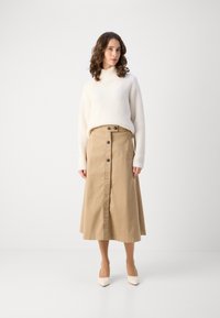 Pulover crem cu model în dungi și guler înalt, asortat cu o fustă bej până la genunchi, cu nasturi pe față și talie cu brâu. Pantofi cu toc simpli, crem.