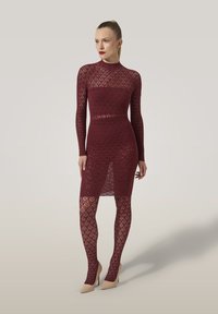 Abito a maglia bordeaux con maniche lunghe e motivo ritagliato, abbinato a collant coordinati con un design in pizzo, completato da tacchi nudi.