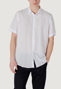 Camisa de botones de manga corta blanca, hecha de tela ligera. Presenta un cuello clásico, placket frontal y un corte relajado con aberturas laterales.