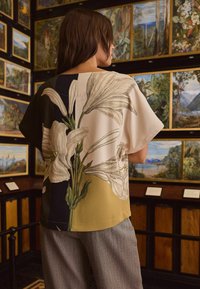 Lilledega blouse, millel on suured valged liiliad kreemi- ja oliivrohelisel taustal. Lühikesed varrukad ja lõdva lõikega. Näha on hallid tekstuuriga püksid.