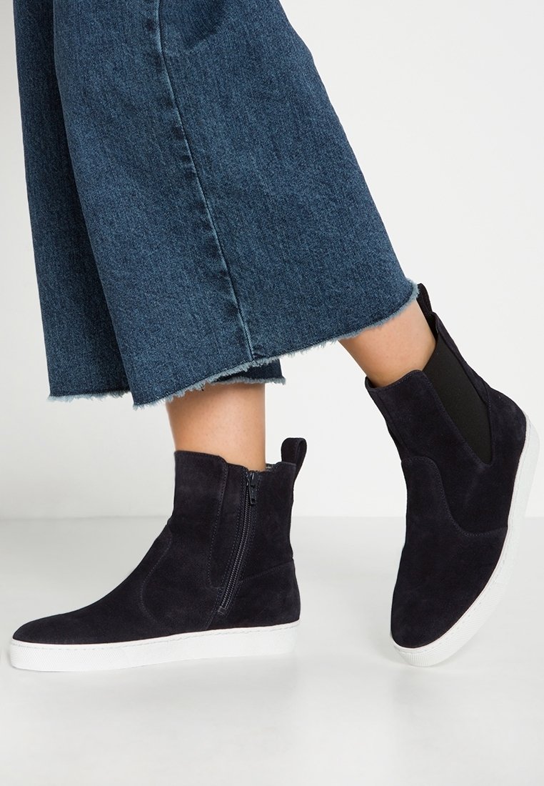 Bottines en suede bleu marine avec fermeture éclair sur le côté et accents élastiques, présentant un dessus texturé et une semelle en caoutchouc blanc.