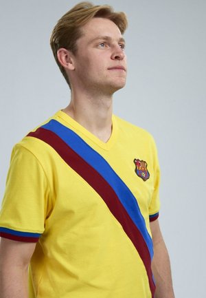 Geel V-hals T-shirt met een diagonale kastanjebruine en blauwe streep. Heeft een meerkleurig clublogo op de borst en contrasterende kleuren voor de manchetten.