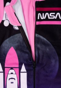 Tuta in pile con accenti rosa, caratterizzata dal logo NASA, design di razzo in bianco e nero, chiusura con zip e texture morbida.