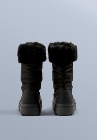 Čierne nepremokavé zimné čižmy majú plyšový, nastaviteľný lem, hladký syntetický vršok a hrubú gumovú podrážku pre lepšiu trakciu.