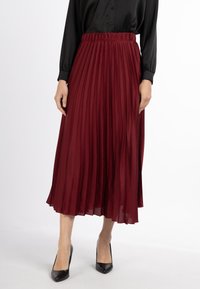 Fustă midi plisată burgundy cu talie elastică, textură de material fluid, asortată cu pantofi cu vârf ascuțit negri.