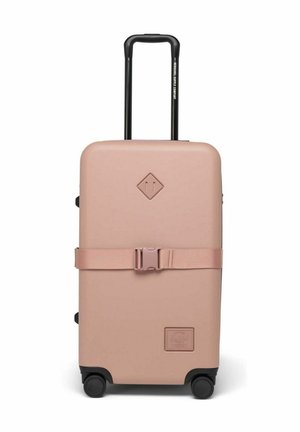 Valise rigide de couleur rose clair матовой avec des roues noires, une poignée rétractable et une sangle horizontale au milieu pour un maintien sécurisé.