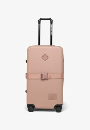 Valise rigide de couleur rose clair матовой avec des roues noires, une poignée rétractable et une sangle horizontale au milieu pour un maintien sécurisé.