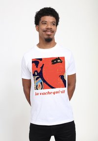 Witte t-shirt met een kleurrijk grafisch ontwerp met de tekst "la vache qui rit," waarop speelse afbeeldingen in oranje en blauwe tinten zijn afgebeeld.
