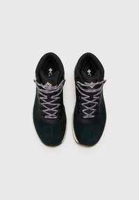 Mørkegrønne suede turstøvler med sorte detaljer, som har lilla snørebånd, metalløyelletter og en lyst farget såle.