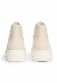 Sneakers alta beige realizzate in materiale sintetico liscio, con una spessa suola bianca e logo impresso sul tallone.