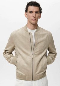 Jachetă bomber din suede bej, cu fermoar frontal, manșete și tiv ribbate, și buzunare laterale, având un design minimalist și textură netedă.