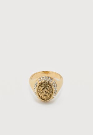 Bague en or avec une gravure détaillée d'une tête de lion entourée de petits pierres précieuses claires sur l'anneau.