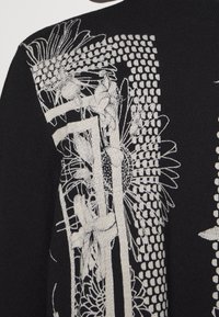 Svart tröja med intrikat vitt blommönster och geometriskt motiv. Texturerat stickat material med olika stygn.