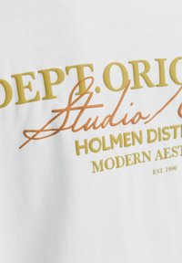 Λευκό ύφασμα με ανάγλυφο κίτρινο κείμενο "DEPT. ORIG," πορτοκαλί καλλιγραφικό "Studio" και κίτρινο κείμενο "HOLMEN DISTRICT MODERN AESTHETIC EST. 1990."