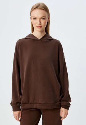 Haut à capuche marron avec une coupe décontractée, texture douce et poche kangourou. Il comprend une capuche avec cordon de serrage, des manches longues et des poignets larges.