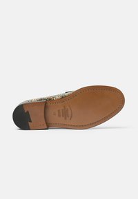Zapato de suela de cuero con un diseño estampado, acentos de cuero marrón, tacón de goma negro y detalle de costura sobre una base lisa.