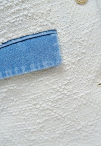 Light blue denim cuff folded over textured off-white tweed fabric with a small visible part of a round beige button.