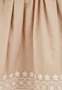 Fény bézs szövet sima textúrával, a szegélyén fehér hímzett virágmintával, amely finom részleteket ad a dizájnhoz.