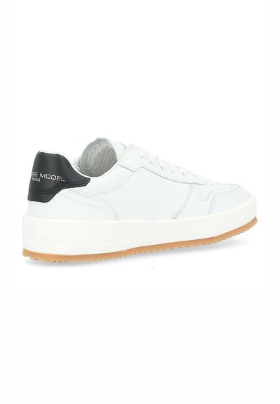 Sneaker bianco in pelle con un tallone nero testurizzato e suola in gomma beige. Presenta lacci rotondi e accenti di design minimalisti.