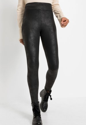 Leggings noirs taille haute avec une finition texturée, présentant un design élégant qui se rétrécit jusqu'aux chevilles, assortis à des bottes noires à lacets.