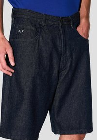 Shorts in denim blu scuro con un taglio classico, design a cinque tasche e cuciture sottili. Include un dettaglio del logo sulla tasca posteriore.