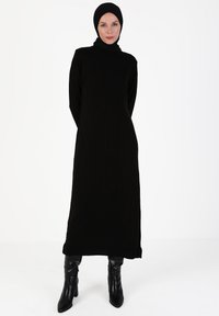 Black knit dress with high neckline, long sleeves, and vertical ribbing texture. Paired with black knee-high heeled boots.