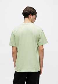 Camiseta de manga corta verde claro, hecha de una tela suave con un corte relajado, que presenta un escote redondo y un diseño simple y sin adornos.