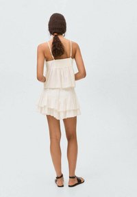 White, tiered dress made of lightweight fabric, featuring thin straps and a ruffled hem. The back showcases a simple design without embellishments.