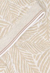 Beige stof met een wit bladpatroon, voorzien van een geribbeld manchet met een bruine accentlijn. Zachte textuur en lichtgewicht materiaal.