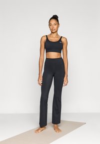 Μαύρο αθλητικό σουτιέν και αντιστοιχίσιμα κολάν με ψηλή μέση, και τα δύο με λεία υφή και εφαρμοστή σχεδίαση. Διακριτό λογότυπο γνωστής μάρκας στο σουτιέν.