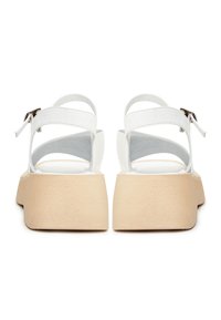 Paire de sandales à plateforme blanches avec semelles épaisses beiges et brides à la cheville avec boucles, vues de dos sur fond blanc.