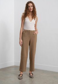 Beige strikket tanktop med dyb V-hals, parret med tanfarvede vidde bukser med sidelommer, glat tekstur og diskrete syninger.