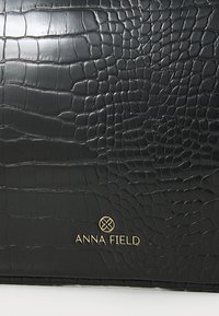Must have nahkaga kott, millel on krokodillimuster. Koti esiküljel on kuldne logo "ANNA FIELD" ning sile viimistlus, mis rõhutab disainielemente.