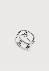 Două inele argintii cu litere decupate din alfabet, pe un fundal simplu și deschis la culoare.