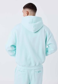 Hoodie in pile verde menta con cappuccio regolabile, vestibilità comoda, polsini e orlo a coste. Presenta una texture liscia e tasca a marsupio.