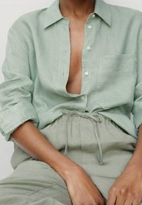 Lichtgroen linnen overhemd met knopen en een borstzak, losse pasvorm en opgerolde mouwen, gecombineerd met bijpassende linnen broek met hoge taille.