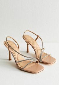 Nude remmar med hög klack och metalliska detaljer, fyrkantig tådesign, slät yta och smal klack.
