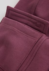 Tissu bordeaux plié avec des coutures visibles et des couches qui se chevauchent, mettant en valeur la texture et le travail soigné des coutures.