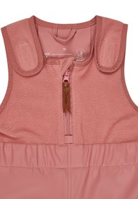 Rosa Kinderoberbekleidung mit einem Oberteil aus Fleece, Reißverschluss und weichen Schulterträgern. Ausgestattet mit einem braunen Lederetikett und einem elastischen Bund.
