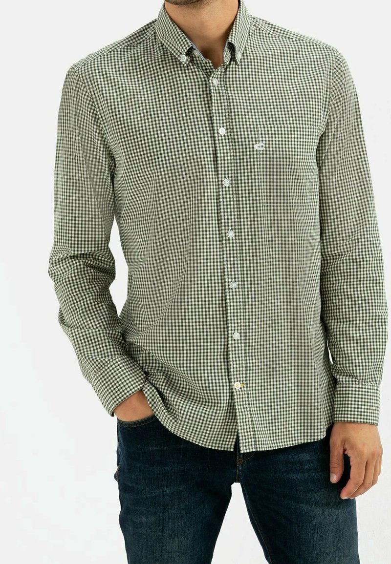 Camisa de cuadros verde y blanca de botones, con mangas largas, un cuello y un bolsillo en el pecho. Llevada con jeans oscuros, la tela parece suave.