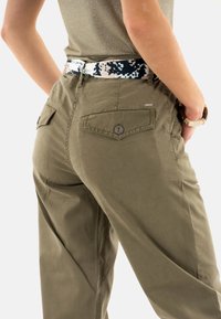 Pantalon vert olive au coupe ample, doté de deux poches arrière et d'une ceinture à motifs noir et blanc. Le tissu semble doux et durable.