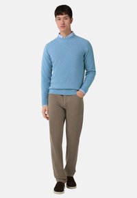 Světlomodrý pletený svetr s žebrovanými manžetami a lemem, kombinovaný s taupe kalhotami a tmavě hnědými botami. Jednoduchý, neformální oděvní soubor.